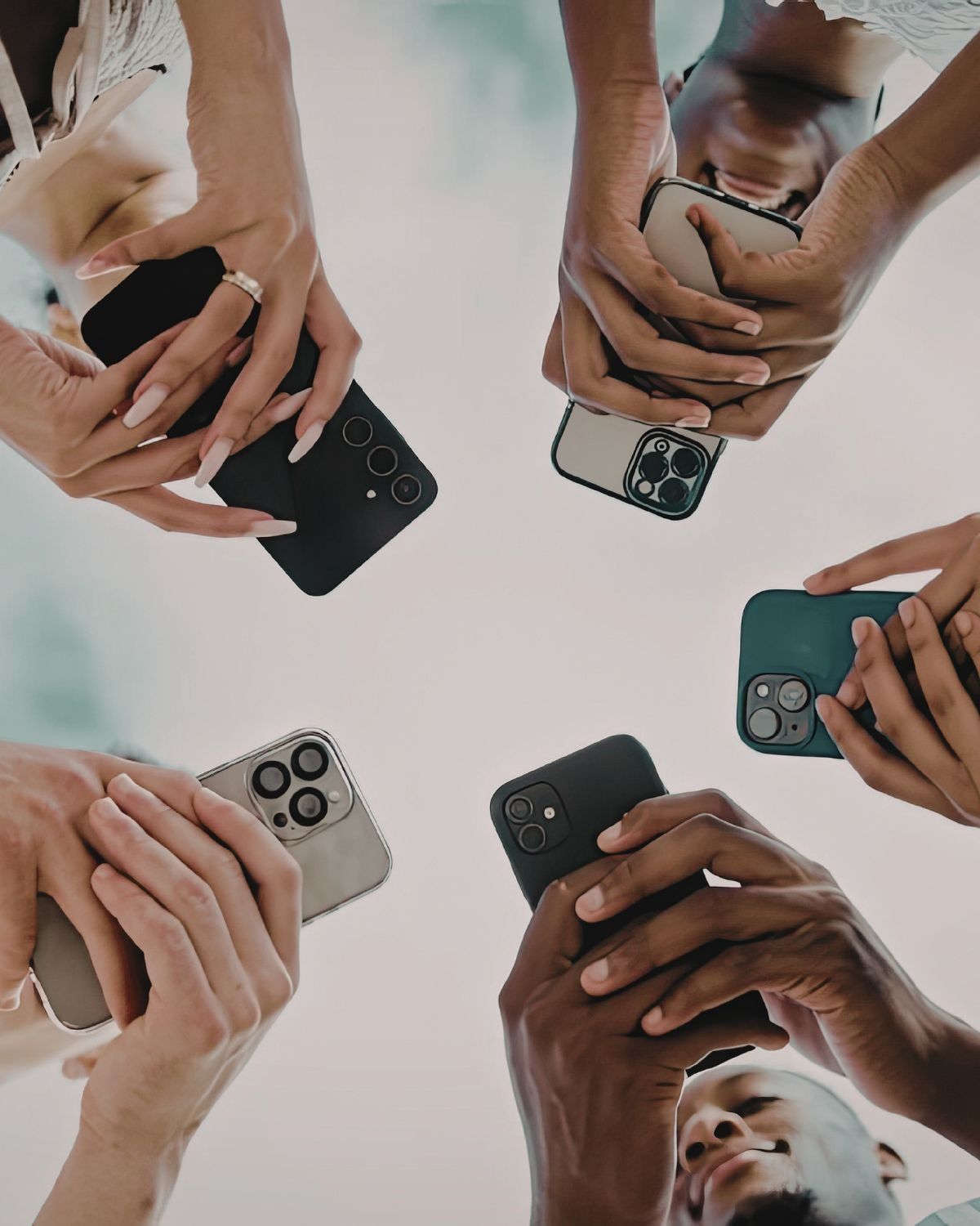 A circle of diverse hands holding phones, faces obscured: the irony of being together and alone.
